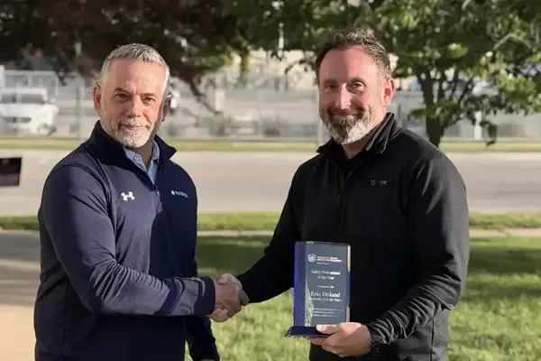 Smiling man in navy quarter-zip shakes hands with Eric Doland, who holds a 'Safety Professional of the Year' award from Notre Dame.